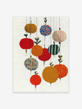 Abstract botanical wall art featuring colorful, textured, fruit-like shapes hanging on strings against a light background.