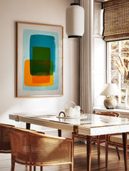 Abstract art print with layered teal, green, and orange rounded rectangles on a light blue, in a styled room mockup