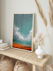 Abstract landscape art print with teal-grey sky, white clouds, and vibrant orange-blue ground, in an alternate framed mockup