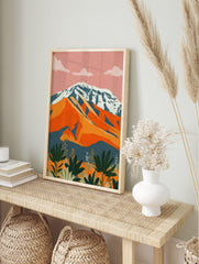 Abstract mountain landscape print with snow-capped peak, orange hills, and green foliage, in an alternate framed mockup