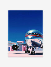 Modern airplane wall art print with a silver and red jet on a tarmac under a blue sky, featuring pink buildings.