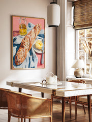 A poster depicting a still life of a baguette, a pat of butter with a knife on a plate, and a bottle of olive oil on a pink surface with a blue and white striped cloth. - Image 2
