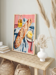 A poster depicting a still life of a baguette, a pat of butter with a knife on a plate, and a bottle of olive oil on a pink surface with a blue and white striped cloth. - Image 4