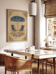 Illustrative beach scene art print with blue and white striped parasol and two deck chairs on beige, in a styled room mockup