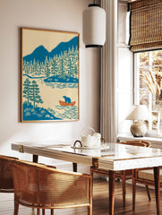 Illustrative print of a blue bear in an orange canoe on a lake with pine trees and blue mountains, in a styled room mockup