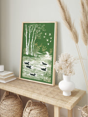 Illustrative green print with white birch trees, golden reeds, black ducks on water, and, in an alternate framed mockup