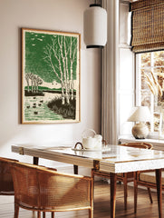 Woodcut style print of white birch trees, ducks on a pond, and flying birds against a green sky, in a styled room mockup