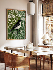 Black and white bird in linocut style perched on branch amidst white flowers and green foliage print, in a styled room mockup