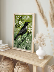 Black bird with white chest and eye on a branch, surrounded by green foliage and white, in an alternate framed mockup