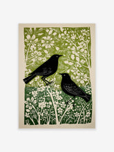 Linocut style print of two black birds amidst green and white flowers and foliage