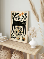 Illustrative black cat and sugar skull wall art with orange and blue floral elements on a, in an alternate framed mockup