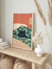 Illustrative print of a black cat with green eyes peeking from a green palm-leaf duvet, in an alternate framed mockup