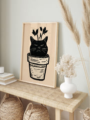 Black cat head in a plant pot with botanical stems, linocut style illustration on cream, in an alternate framed mockup