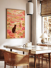 Illustrative print of black cat in colourful landscape with pink hills, green trees, and distant, in a styled room mockup