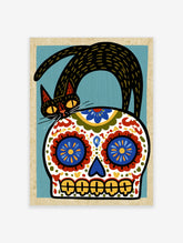 Stylized black cat standing on a decorative Mexican sugar skull with blue, red, and yellow floral patterns on blue background