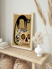 Black cat perched on a floral patterned Mexican sugar skull, illustrative art print on a, in an alternate framed mockup