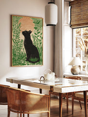 Black cat silhouette looking at a large orange moon in a field of green plants, illustrative print, in a styled room mockup