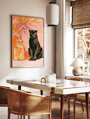 Black panther sitting beside a vase of vibrant orange and pink tropical leaves on a pink, in a styled room mockup