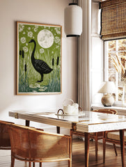 Black swan standing in a pond with white reeds, lily pads, and flowers under a full moon on a green, in a styled room mockup