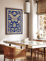 Blue and cream illustrative print of a moth and beetle surrounded by ornate botanical flowers and, in a styled room mockup