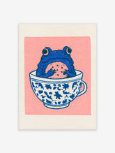 Illustrative blue frog sitting in a patterned teacup holding a cookie against a solid pink background art print