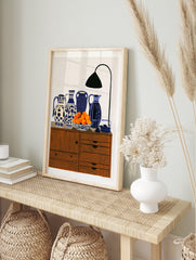 Still life art print featuring four patterned blue and white vases, a bowl of oranges, and a, in an alternate framed mockup