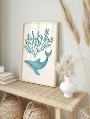 Blue watercolour whale swimming below teal seaweed illustration on white background, in an alternate framed mockup