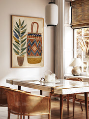 Illustrative wall art print of a tall potted plant next to a geometric patterned woven basket in, in a styled room mockup