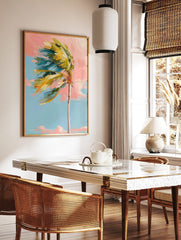 Impressionistic palm tree with green and yellow leaves blowing left against a pink and blue sky, in a styled room mockup