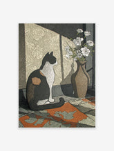 Illustrative calico cat wall art print sitting next to a vase of white flowers, with sunlight casting shadows on patterned wallpaper.