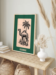 Black line art illustration of a camel and palm tree on beige, with a dark green border, in an alternate framed mockup
