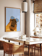 Stylised capybara illustration wearing blue-tinted sunglasses against a light blue background, in a styled room mockup