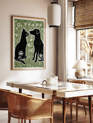 Black cat and dog silhouettes facing each other in green grass with white flowers, linocut style, in a styled room mockup