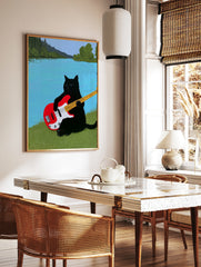 Black cat playing a red electric bass guitar on a grassy riverbank with a blue river and trees, in a styled room mockup