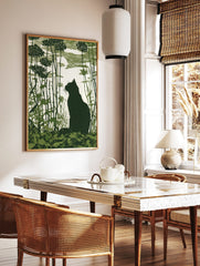 Green linocut print of a black cat silhouette in tall foliage looking at a moon in a textured sky, in a styled room mockup