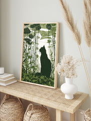 Dark green linocut-style print of a cat silhouette in a garden with tall plants and a moon, in an alternate framed mockup