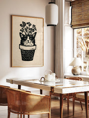Linocut style illustration of a cat face emerging from a plant pot with clover leaves, black and, in a styled room mockup