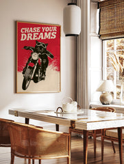 Black cat wearing motorcycle goggles on a bike with red background and the text Chase Your Dreams, in a styled room mockup
