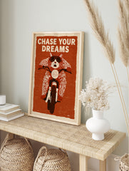 Illustration of a cat wearing goggles on a motorcycle with the text Chase Your Dreams on a, in an alternate framed mockup