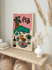 Illustrative green chameleon on a table with food, drinks, a plant, and Japanese characters, in an alternate framed mockup