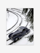 Navy blue classic car on snow-covered train tracks, high-angle view with pine branches and curving rails