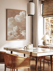 Warm sepia-toned photographic print of large, layered cumulus clouds against a soft sky, in a styled room mockup