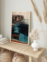 Coastal cliff wall art with dark rugged rock formations and vibrant turquoise water in an, in an alternate framed mockup