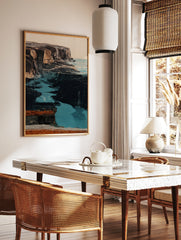 Coastal cliff wall art with dark rugged rock formations and vibrant turquoise water in an, in a styled room mockup