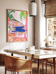 Colourful illustrative wall art of a coastal village with boats in a blue harbour and palm trees, in a styled room mockup