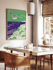 Illustrative coastal wall art with a white seagull flying over a green cliffside village and purple ocean. - Image 2