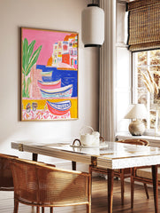 Colourful illustrative coastal town art print with boats in blue water, white buildings, and green, in a styled room mockup