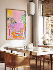 Illustrative print of a colourful coastal town with pink sea, yellow boats, and green palm trees, in a styled room mockup