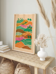 Colourful illustrative landscape art print with rolling hills, patterned green, orange, and, in an alternate framed mockup