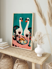 Two white geese in sunglasses at a pink table with wine and food, against a teal background, in an alternate framed mockup